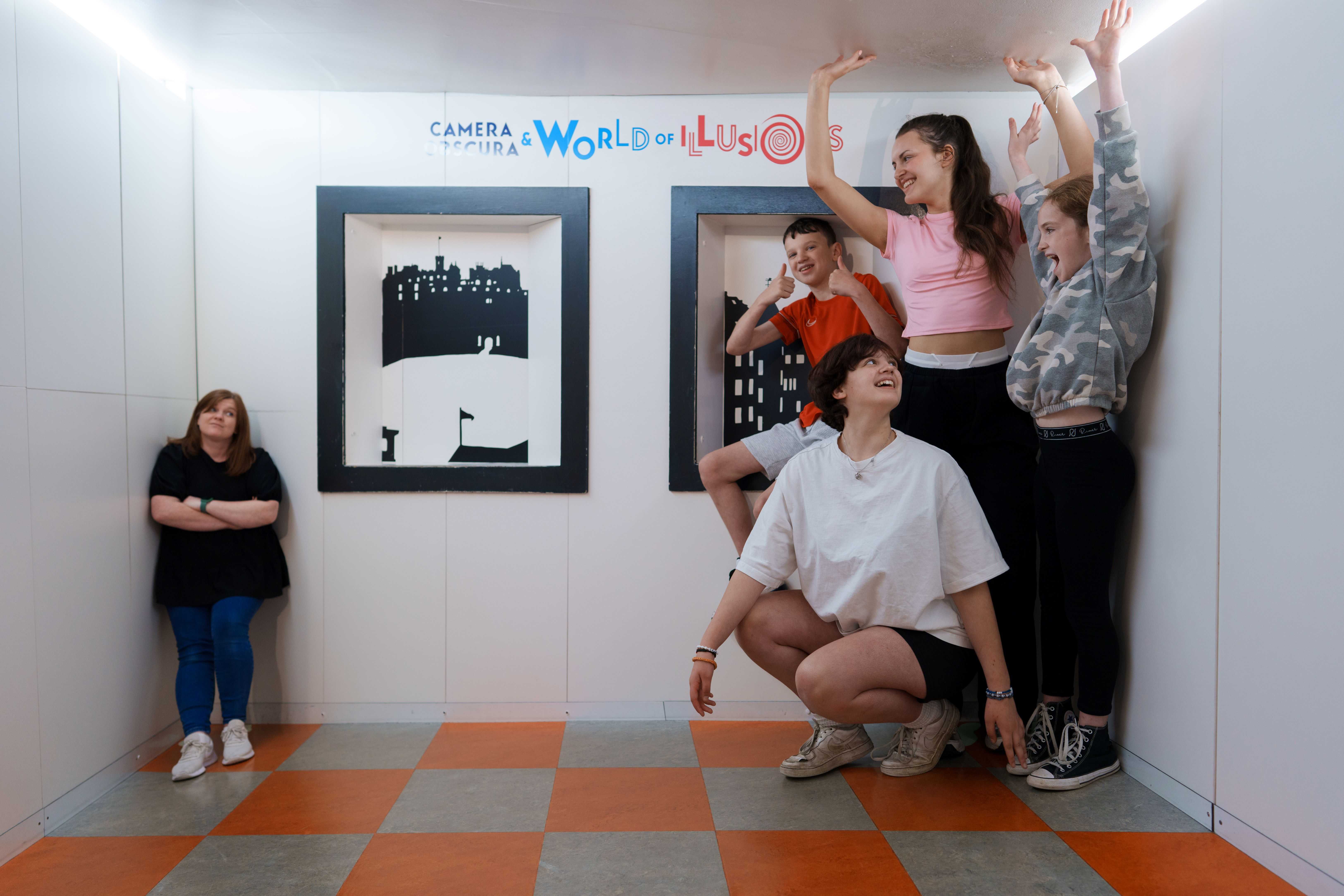 At the Camera Obscura in Edinburgh, a group of 5 people are indoors, looking at optical illusion.